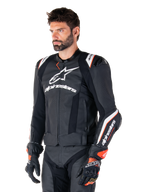 Modello uomo che indossa la giacca in pelle Alpinestars Missile V3 Ignition, nero con accenti bianchi e arancioni, caratterizzata da loghi bianchi evidenti, sezioni in pelle traforata e protezioni sulle spalle, abbinata a guanti da corsa per un look sportivo da gara.