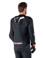 Giacca in pelle Alpinestars Missile V3 Ignition, vista posteriore, nero con accenti bianchi e rossi, con gobba aerodinamica sportiva sottile e marchio Alpinestars, indossata con pantaloni in pelle coordinati e guanti da corsa
