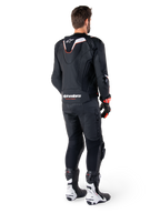 Vista posteriore di un pilota che indossa la giacca in pelle Alpinestars Missile V3 Ignition in nero, con gobba aerodinamica sportiva sottile con accenti bianchi e rossi, marchio Alpinestars sulla parte bassa della schiena, abbinata a pantaloni in pelle neri coordinati e stivali da corsa bianchi e neri, completo sportivo professionale da moto