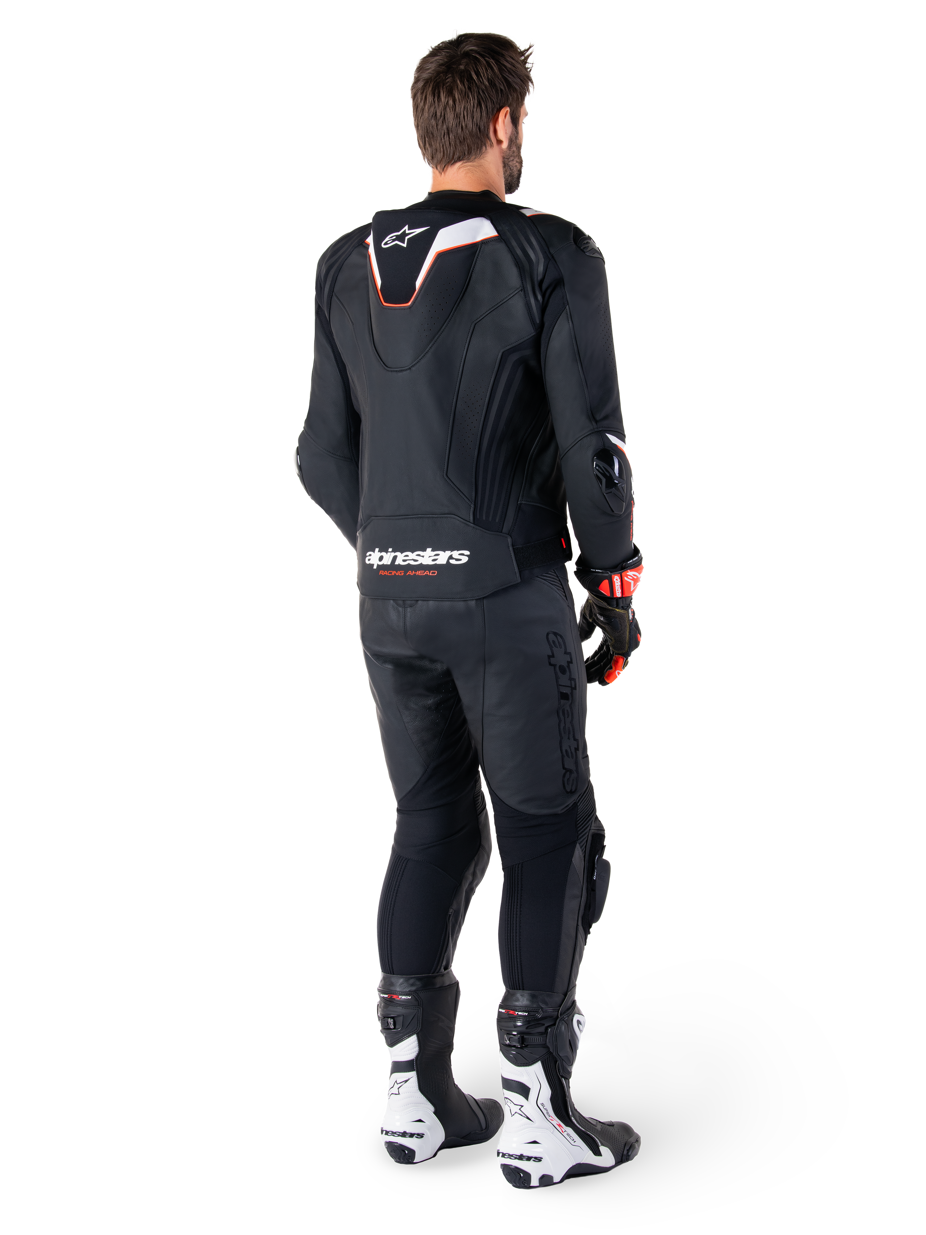 Vista posteriore di un pilota che indossa la giacca in pelle Alpinestars Missile V3 Ignition in nero, con gobba aerodinamica sportiva sottile con accenti bianchi e rossi, marchio Alpinestars sulla parte bassa della schiena, abbinata a pantaloni in pelle neri coordinati e stivali da corsa bianchi e neri, completo sportivo professionale da moto