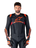 Giacca in pelle Alpinestars Missile V3 Ignition, giacca da moto racing, nero e rosso fluo, indossata con guanti da corsa e pantaloni in pelle coordinati, con ventilazione traforata e logo Alpinestars in evidenza, abbigliamento da corsa professionale