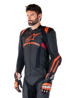 Giacca in pelle Alpinestars Missile V3 Ignition, nero con accenti rosso fluo e rosso scuro, indossata da un modello uomo con guanti da corsa e pantaloni in pelle abbinati, con logo Alpinestars evidente, pannelli in pelle traforata e protezioni esterne per le spalle, abbigliamento professionale da gara motociclistica