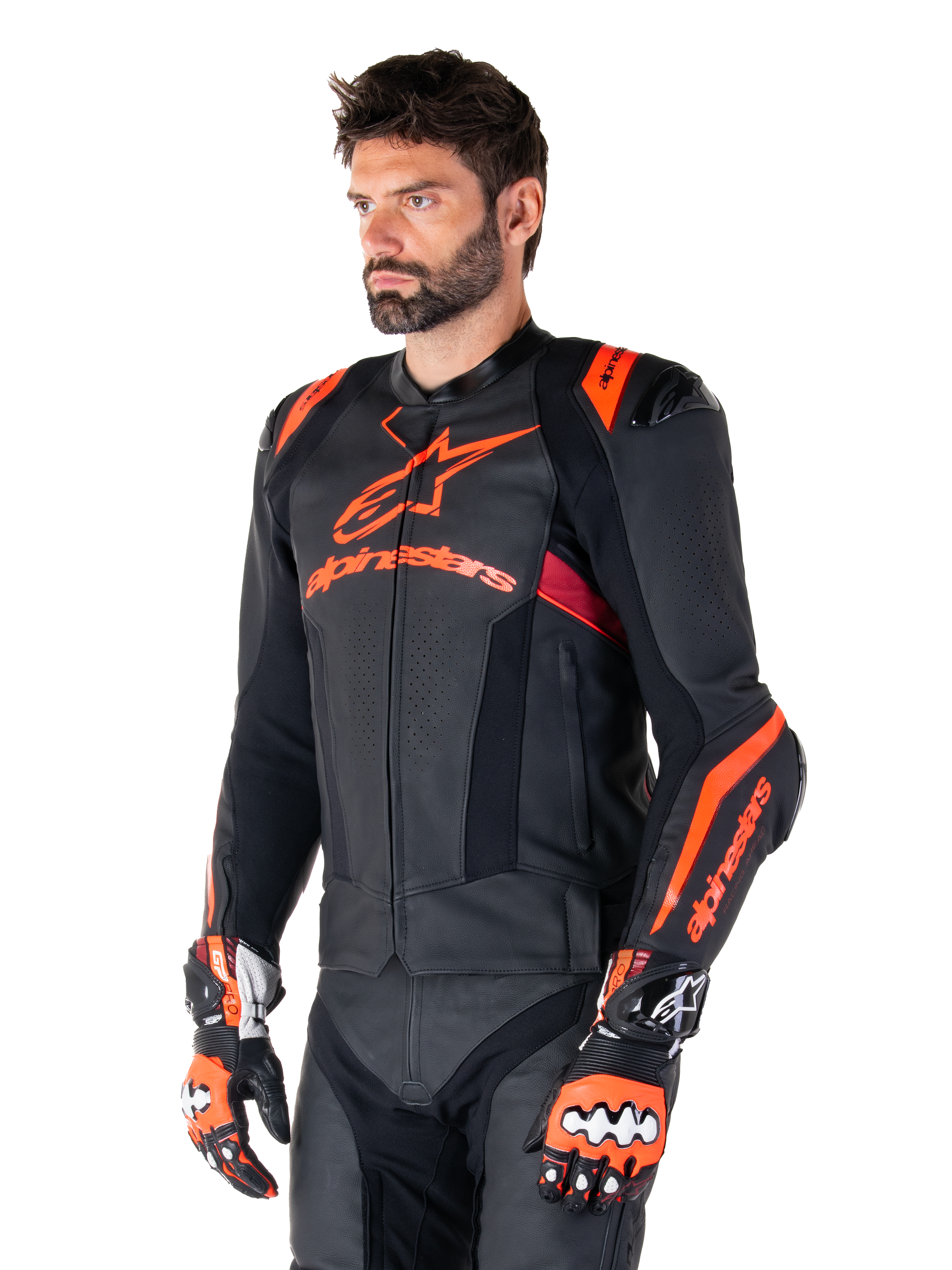 Giacca in pelle Alpinestars Missile V3 Ignition, nero con accenti rosso fluo e rosso scuro, indossata da un modello uomo con guanti da corsa e pantaloni in pelle abbinati, con logo Alpinestars evidente, pannelli in pelle traforata e protezioni esterne per le spalle, abbigliamento professionale da gara motociclistica