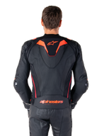 Giacca in pelle Alpinestars Missile V3 Ignition, vista posteriore, nero con accenti rosso fluo e rosso scuro, con gobba aerodinamica sportiva e logo Alpinestars sulla schiena, indossata con pantaloni coordinati in pelle nera, abbigliamento tecnico da competizione motociclistica