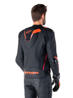 Giacca in pelle Alpinestars Missile V3 Ignition, giacca sportiva da corsa da uomo, nero con dettagli rosso fluo, vista posteriore con la sottile gobba sportiva aerodinamica e marchio Alpinestars sulla parte bassa della schiena, indossata con pantaloni in pelle neri e guanti da corsa, design motorsport professionale ed elegante