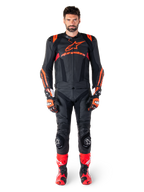 Modello maschile che indossa la giacca in pelle Alpinestars Missile V3 Ignition in Nero Rosso Fluo Rosso Scuro, equipaggiamento completo da gara motociclistica con pantaloni in pelle coordinati, guanti da corsa e stivali, caratterizzato dal logo Alpinestars sul petto, posa frontale, abbigliamento professionale per guida sportiva