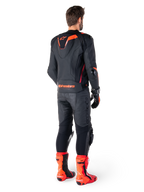 Alpinestars Missile V3 Ignition Leather Jacket, giacca da moto racing sportiva, nero e rosso fluo, vista posteriore di un pilota con completo da gara, pantaloni in pelle coordinati, guanti e stivali rossi, caratterizzata da gobba sportiva Aero-hump e logo sulla parte bassa della schiena.