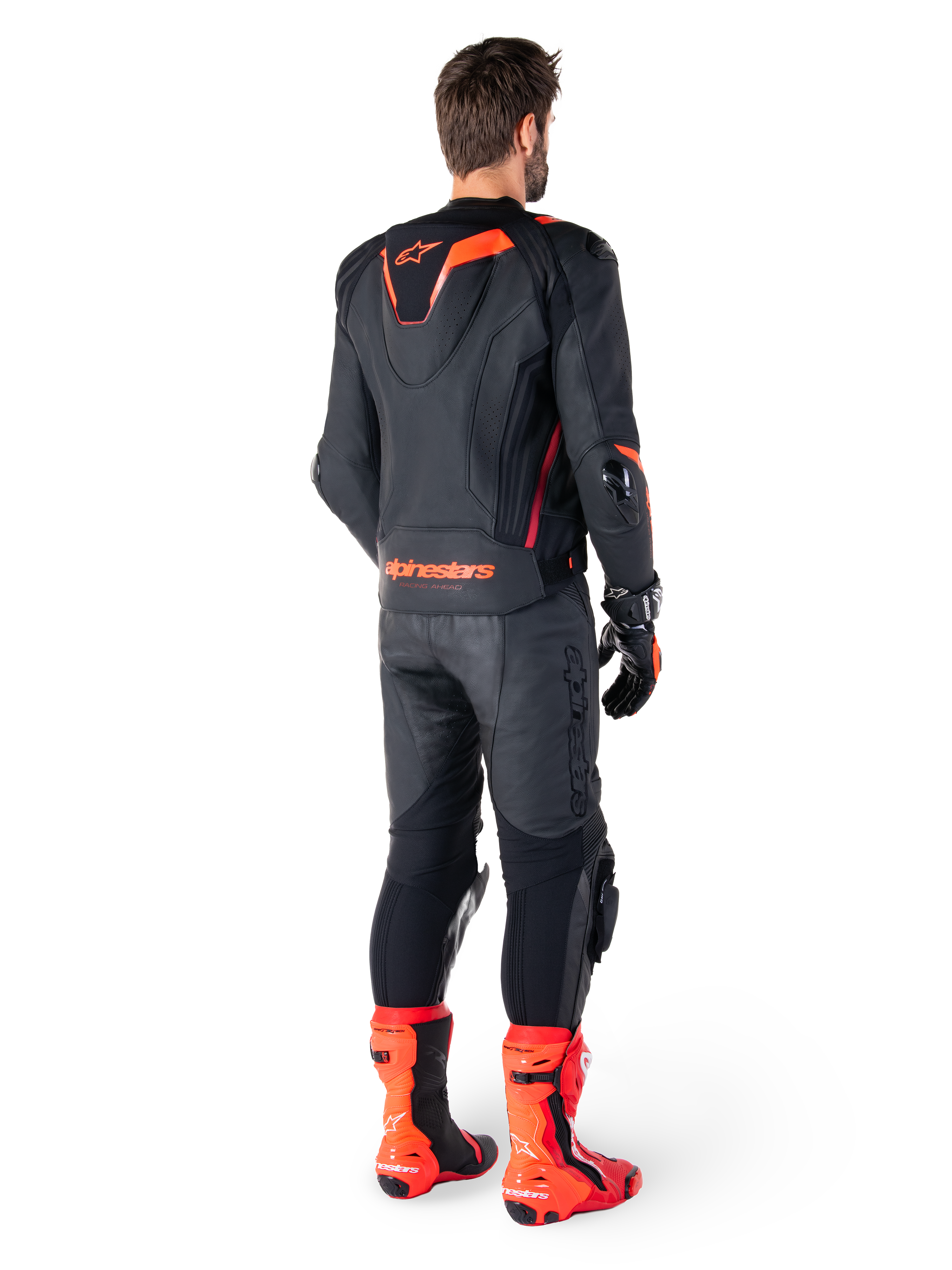 Alpinestars Missile V3 Ignition Leather Jacket, giacca da moto racing sportiva, nero e rosso fluo, vista posteriore di un pilota con completo da gara, pantaloni in pelle coordinati, guanti e stivali rossi, caratterizzata da gobba sportiva Aero-hump e logo sulla parte bassa della schiena.