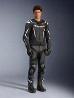 Giacca in pelle Alpinestars GP Force V2 Air in nero e bianco, indossata da un pilota uomo con pantaloni racing, guanti e stivali neri coordinati, con pannelli in pelle traforata, accenti bianchi e logo Alpinestars rosso sul petto, abbigliamento sportivo da moto