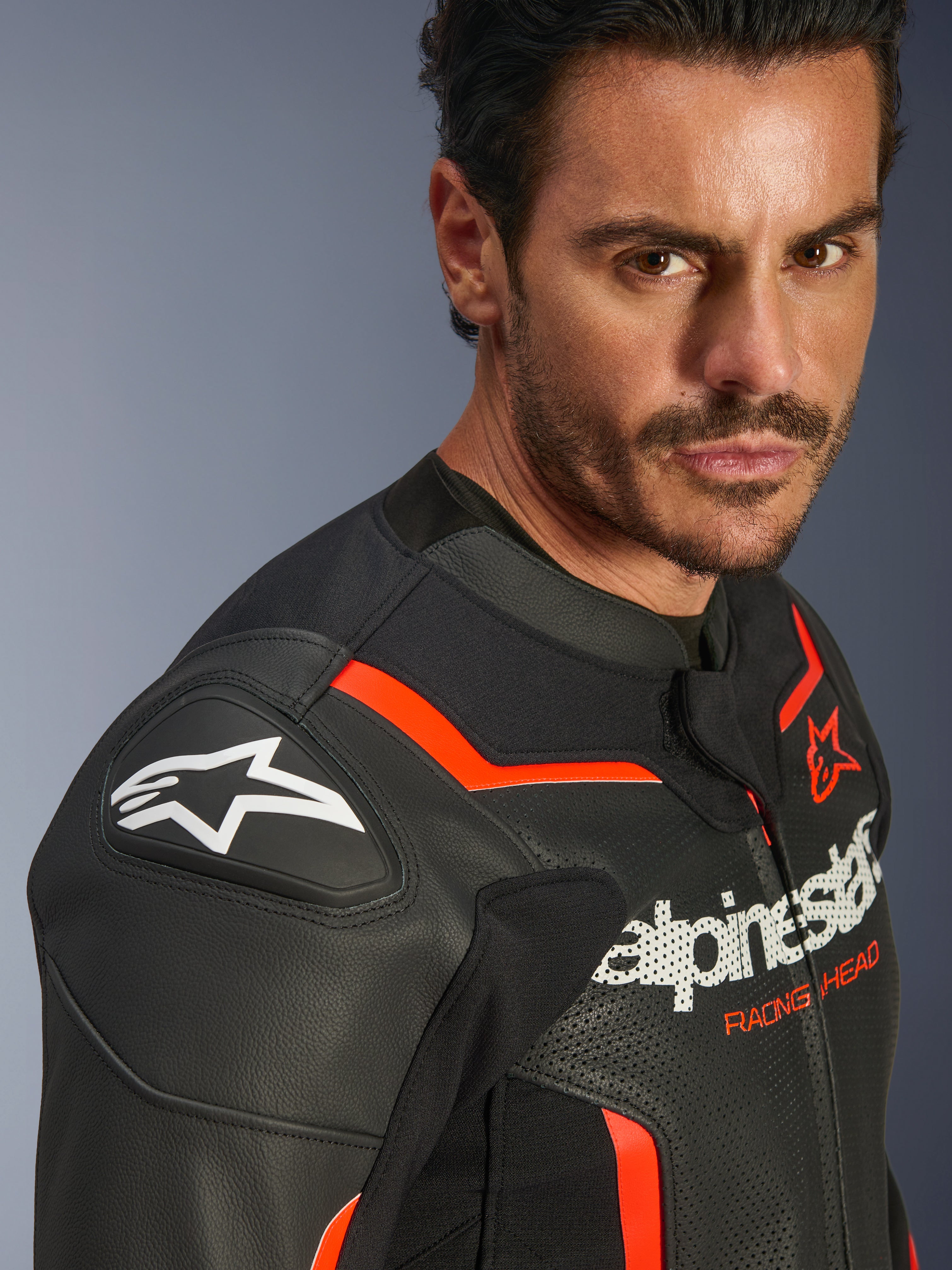 Giacca in pelle Alpinestars GP Force V2 Airflow, nero e rosso fluo, indossata da un modello, caratterizzata da pelle traforata, slider sulle spalle GP Lite Evo DFS e branding con logo Alpinestars, abbigliamento protettivo per moto sportiva