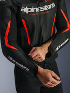 Alpinestars GP Force V2 Air Leather Jacket, giacca in pelle in nero e rosso fluo, primo piano della costruzione in pelle traforata, loghi bianchi su petto e maniche, e un pilota che regola la zip dell'avambraccio per una vestibilità personalizzata.