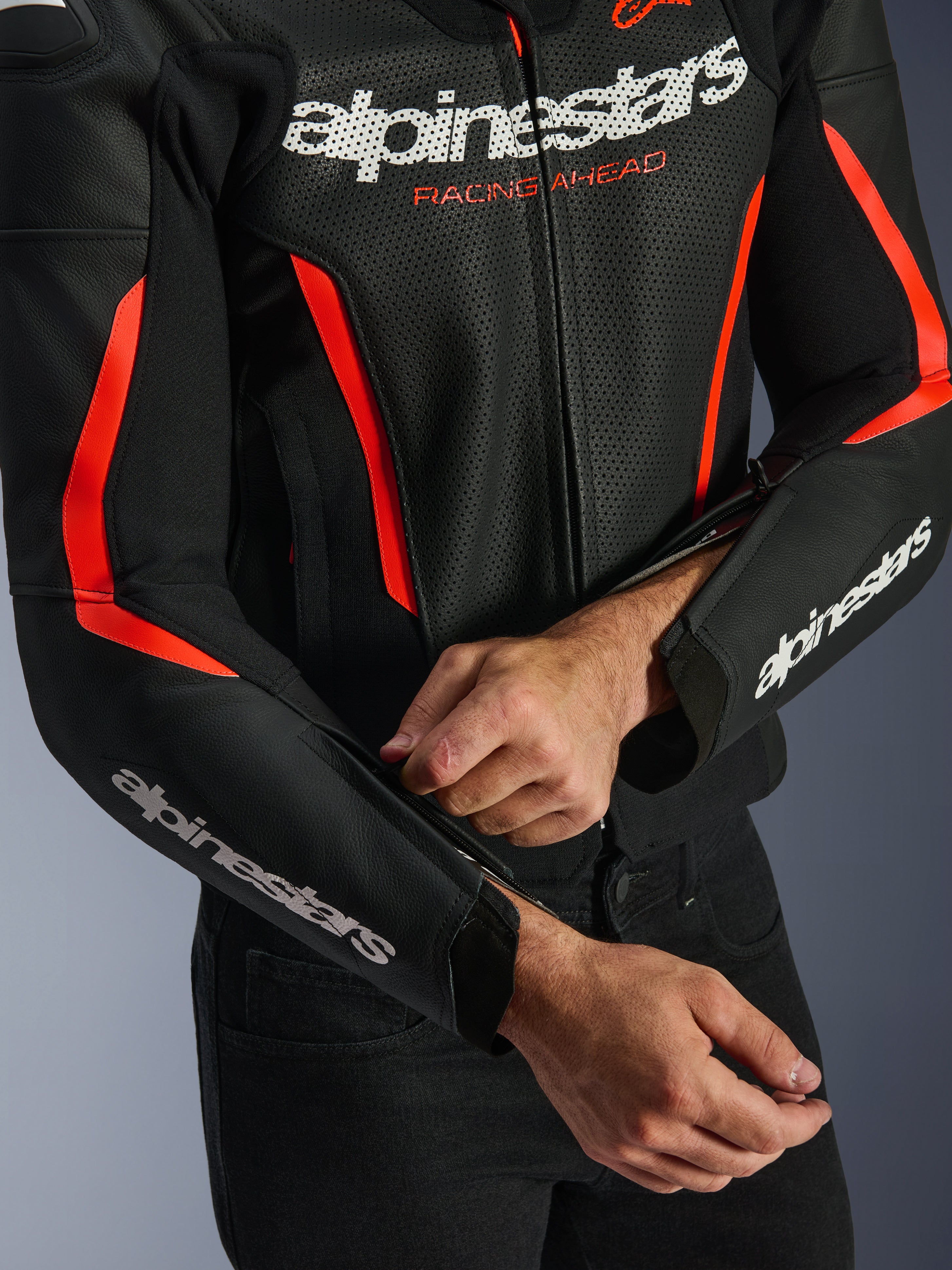 Alpinestars GP Force V2 Air Leather Jacket, giacca in pelle in nero e rosso fluo, primo piano della costruzione in pelle traforata, loghi bianchi su petto e maniche, e un pilota che regola la zip dell'avambraccio per una vestibilità personalizzata.