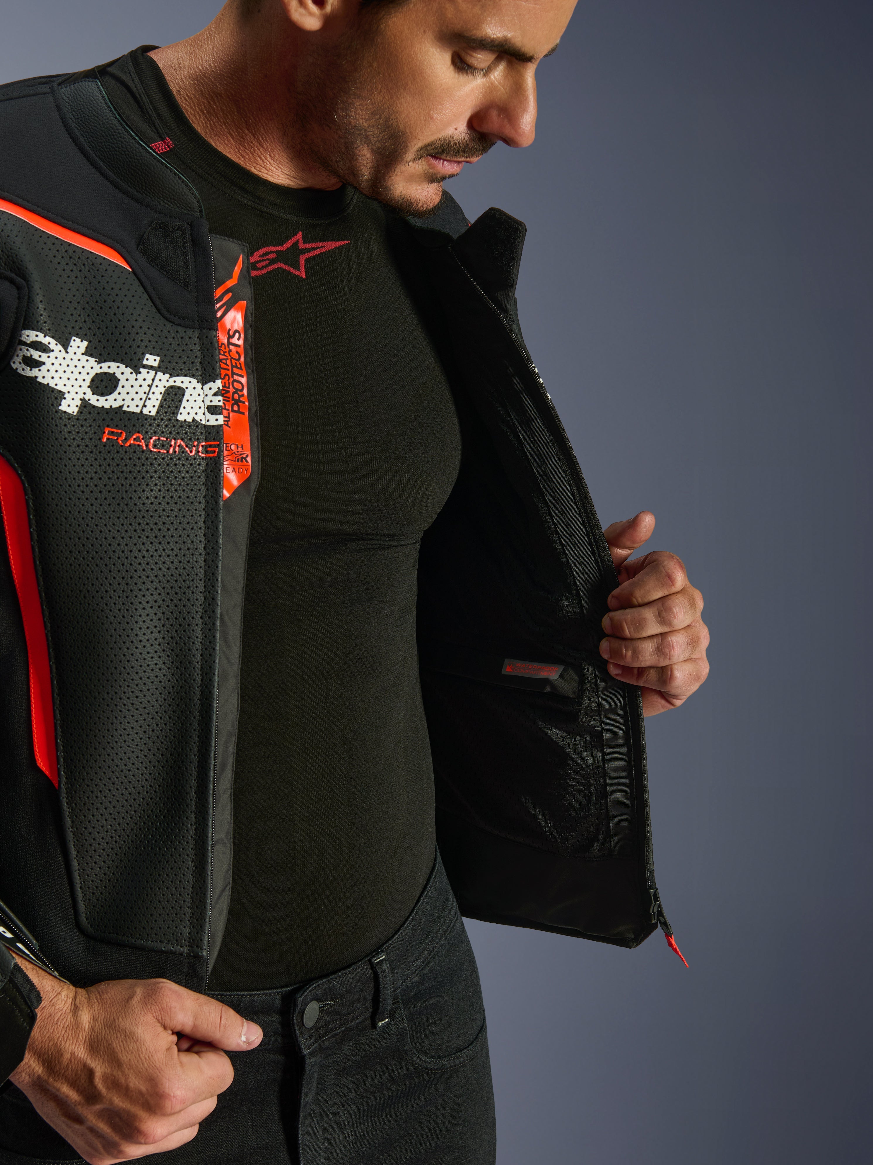 Giacca in pelle Alpinestars GP Force V2 Air, nero e rosso fluo, aperta per mostrare la tasca impermeabile interna e il marchio, costruzione multi-pannello in pelle traforata per il flusso d'aria, indossata con base layer Alpinestars nero
