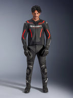 Modello che indossa la giacca in pelle Alpinestars GP Force V2 Air in nero e rosso fluo, con pannelli traforati sul petto e loghi bianchi, abbinata a pantaloni in pelle da moto neri, guanti neri e stivali neri per un look racing completo.