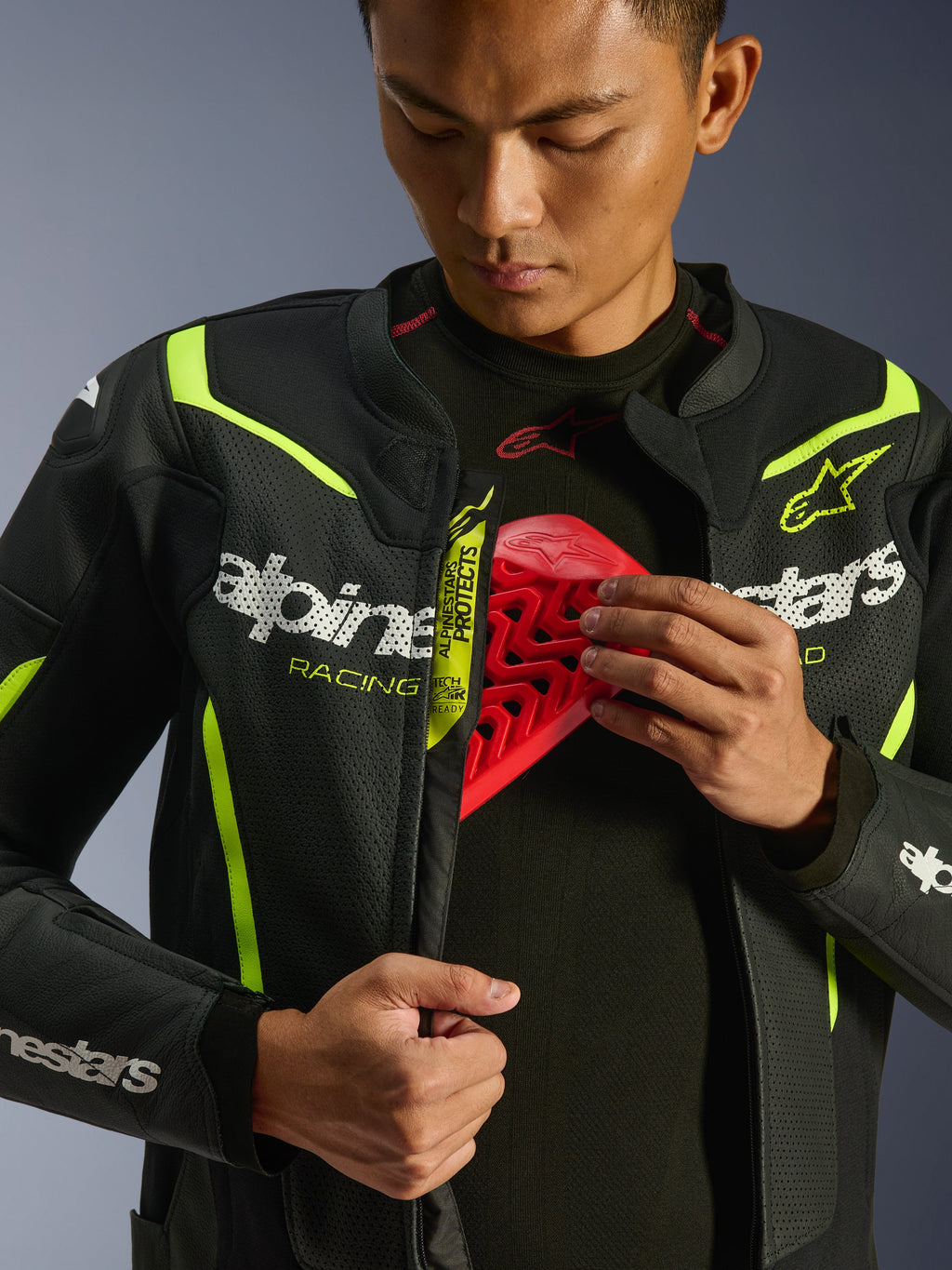 Giacca in pelle Alpinestars GP Force V2 Air, nero e giallo fluo, giacca da moto in pelle traforata, indossata da un pilota che mostra lo scomparto per la protezione toracica con un inserto rosso, con loghi Alpinestars bianchi e ampie perforazioni per il flusso d'aria.