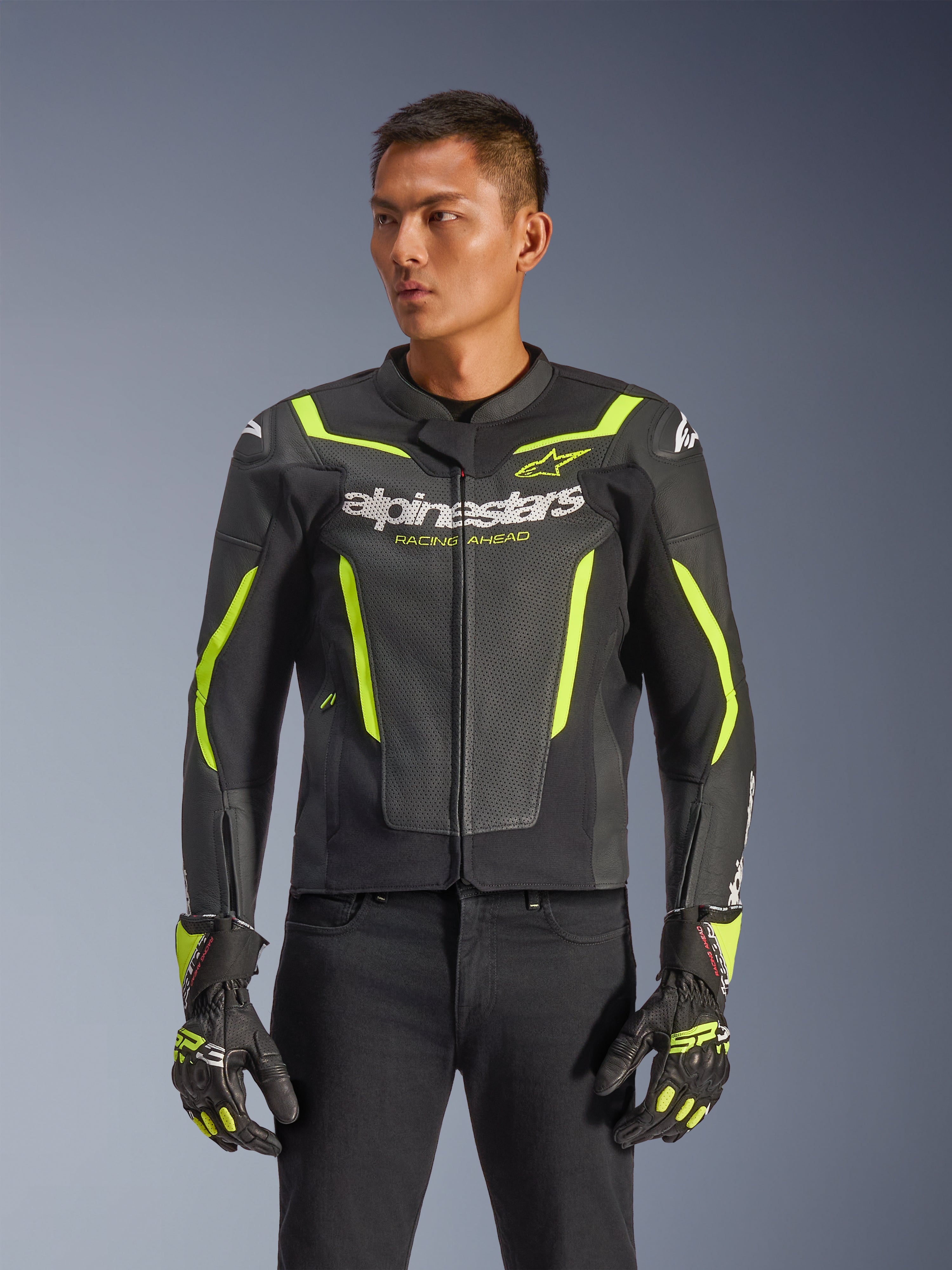 Giacca in pelle Alpinestars GP Force V2 Air, nero e giallo fluo, giacca da moto in pelle traforata con protezioni e accenti neon, indossata con guanti da corsa coordinati e pantaloni neri, vestibilità sportiva con loghi evidenti