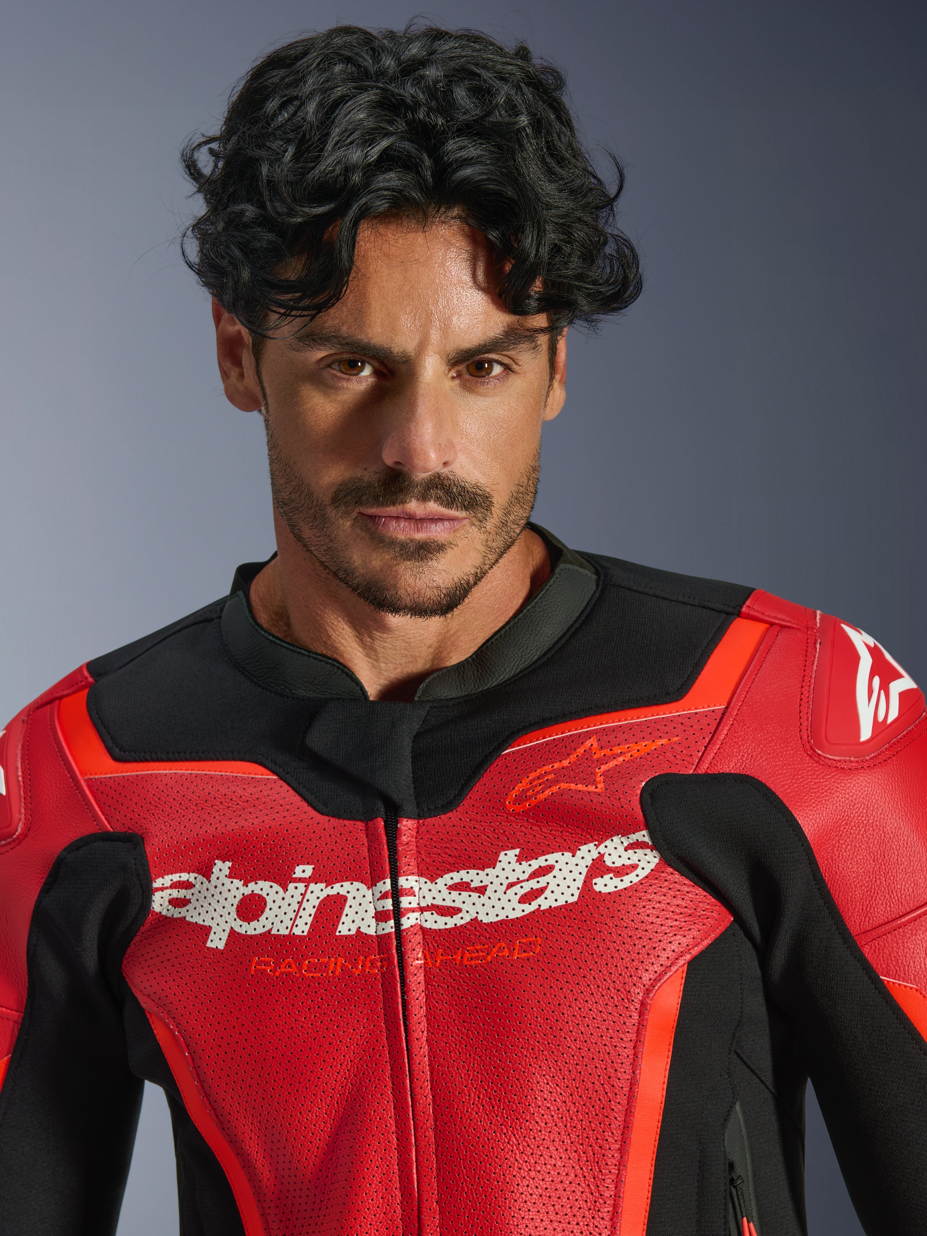 Giacca in pelle Alpinestars GP Force V2 Air, rosso e rosso fluo, indossata da un modello uomo, con logo Alpinestars bianco e scritta 'Racing Ahead' sul petto, pelle traforata per la ventilazione, abbigliamento moto stile sportivo