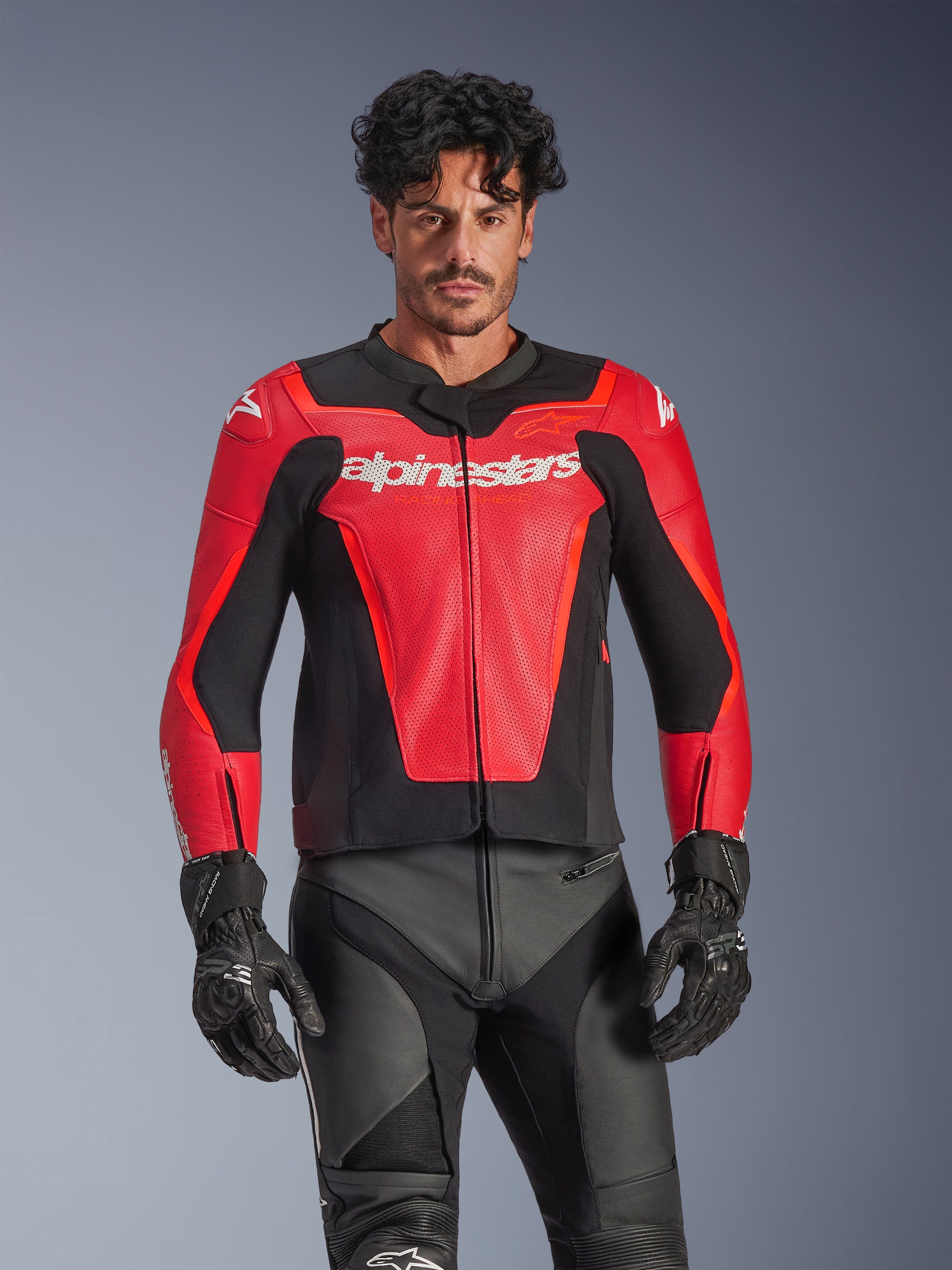Alpinestars GP Force V2 Air Leather Jacket, giacca da moto racing rossa e nera, costruzione in pelle traforata con logo Alpinestars bianco, indossata da un modello e abbinata a pantaloni e guanti da corsa neri