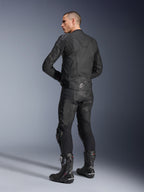 Giacca in pelle Alpinestars Dusk, nera, vista posteriore a tre quarti su un modello che indossa pantaloni da moto in pelle coordinati e stivali da corsa performanti, con pannelli a fisarmonica in pelle, logo a stella Alpinestars argento sulla parte inferiore della schiena e branding DUSK sulla parte superiore, scatto professionale in studio