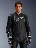 Giacca in pelle Alpinestars Dusk, nero e bianco, giacca da moto in pelle con zone di protezione imbottite e loghi bianchi, indossata con guanti da corsa neri e bianchi con accenti rossi, abbigliamento sportivo professionale da moto