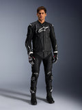 Alpinestars Missile V3 Leather Pants, neri, indossati da un pilota uomo come parte di un completo da corsa in pelle, con loghi Alpinestars bianchi, saponette protettive sulle ginocchia, stivali e guanti da gara.