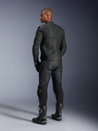 Pantaloni in pelle Alpinestars Missile V3 e giacca in pelle Dusk, nero con dettagli oro, vista posteriore del pilota, con loghi a rilievo e pannelli elasticizzati a soffietto, indossati con stivali e guanti Supertech R neri, abbigliamento professionale da motorsport.