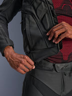 Alpinestars Dusk Leather Jacket, nera, primo piano della cerniera di collegamento in vita fissata ai pantaloni da moto in pelle, indossata con un base layer a fantasia rossa e nera, robusta costruzione in pelle per la guida su strada.