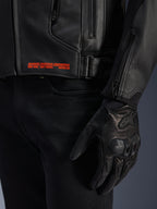 Giacca in pelle Alpinestars GP Plus V4, nero, primo piano del dettaglio laterale con testo del brand arancione 'ADVANCED RACEWEAR ENGINEERING', fibbia regolabile e guanto da moto in pelle nera, abbigliamento sportivo da moto