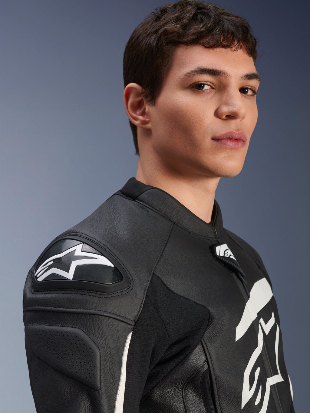 Giacca in pelle Alpinestars GP Plus V4, nero e bianco, indossata da un modello, con logo Alpinestars bianco e slider sulle spalle DFS, struttura in pelle di derivazione racing per guida sportiva