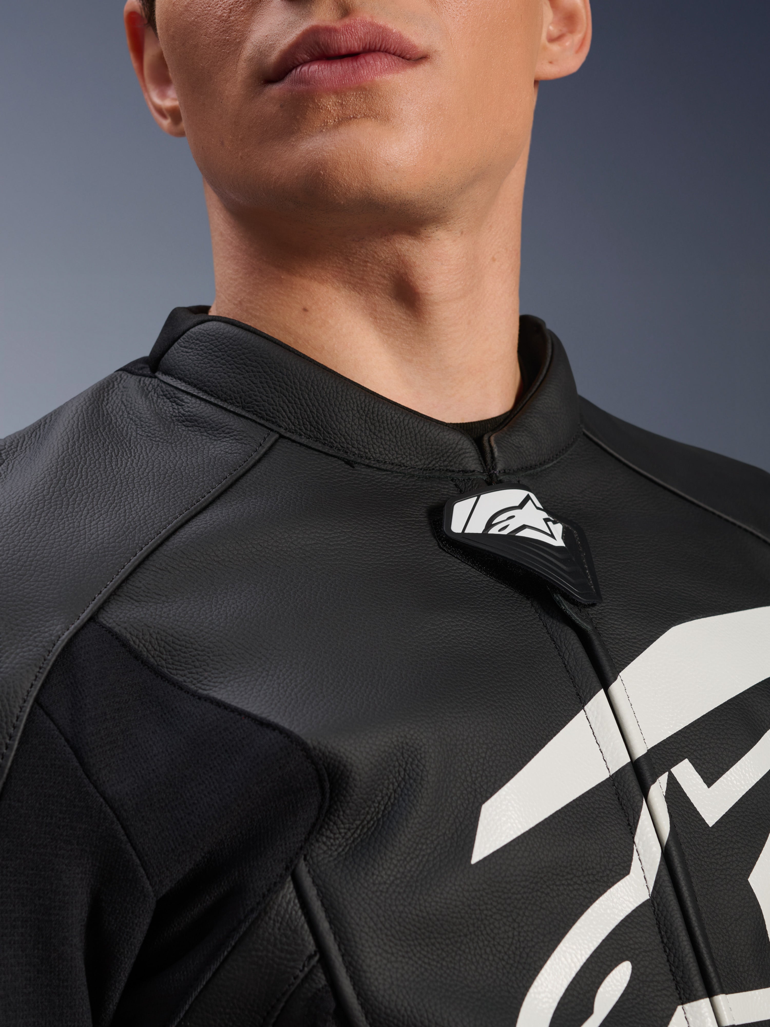 Giacca in pelle Alpinestars GP Plus V4, giacca da moto sportiva, nero e bianco, primo piano del colletto in pelle testurizzata e della linguetta con logo Alpinestars, grafica bianca sul petto, design di derivazione racing
