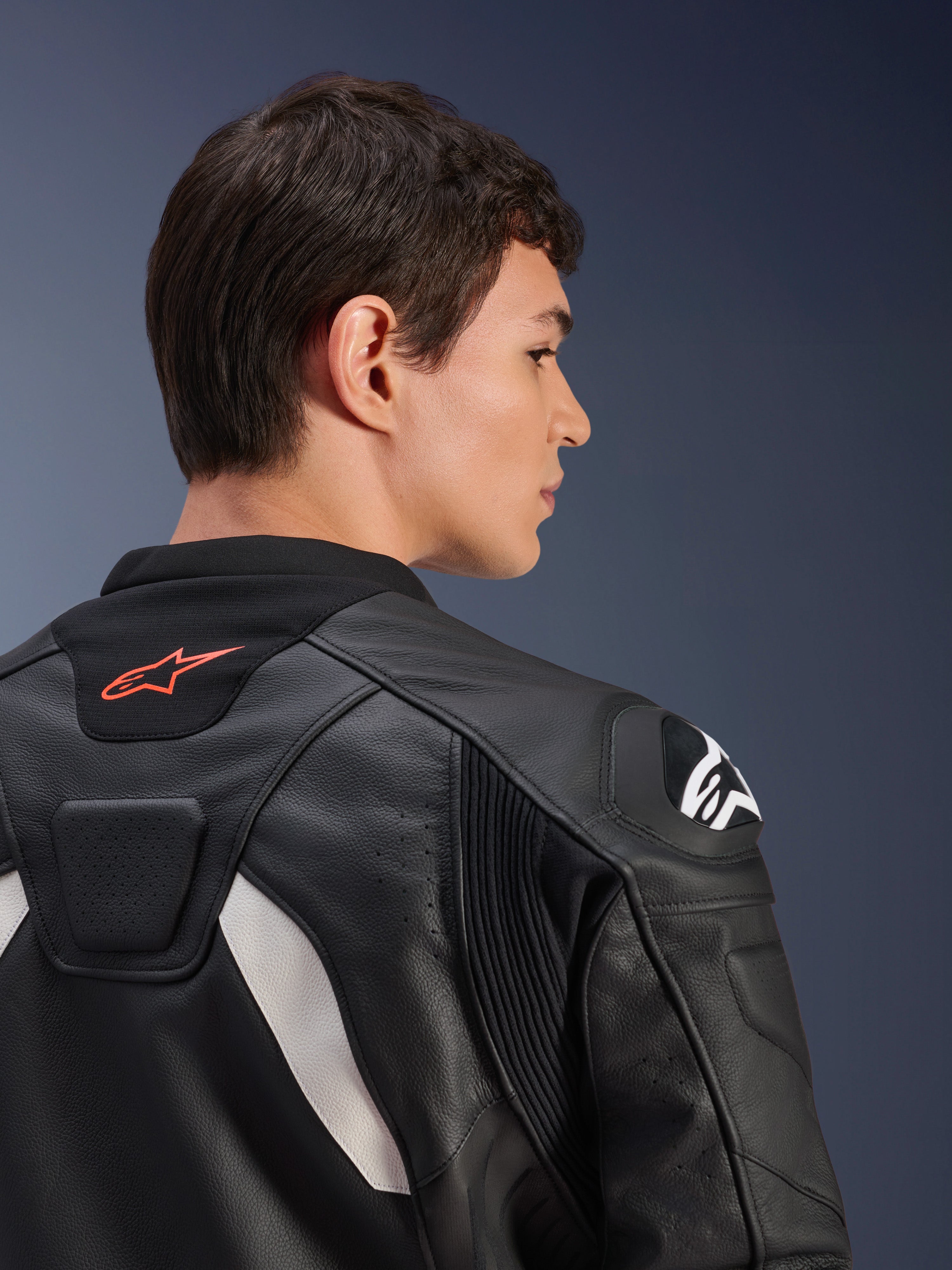 Giacca in pelle Alpinestars GP Plus V4, nero e bianco, vista posteriore ravvicinata di un modello che indossa la giacca, caratterizzata da un logo rosso sul colletto, protezioni bianche sulle spalle e costruzione in pelle resistente con pannelli elasticizzati