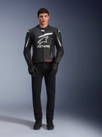 Modello che indossa la giacca in pelle Alpinestars GP Plus V4, nero e bianco, con vistoso marchio Astars bianco sul petto e dettagli bianchi sulle spalle, abbinata a guanti e pantaloni da moto neri, abbigliamento da moto sportivo ed elegante