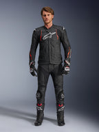 Pilota uomo con giacca in pelle Alpinestars Dusk Airflow in nero rosso fluo, con pannelli in pelle traforata e logo bianco sul petto, abbinata a pantaloni in pelle nera coordinati, saponette, guanti e stivali racing, outfit completo da moto stradale