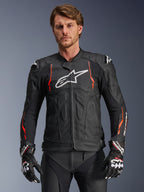Alpinestars Dusk Airflow Leather Jacket, giacca racing in pelle nera con accenti rosso fluo e bianchi, dotata di ampie perforazioni per la ventilazione, logo bianco sul petto e slider esterni sulle spalle, indossata da un modello con guanti racing coordinati
