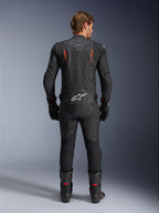 Giacca in pelle Alpinestars Dusk Airflow, nero e rosso fluo, vista posteriore che mostra le ampie perforazioni e il grande logo bianco sulla parte bassa della schiena, indossata con abbigliamento racing in pelle coordinato, inclusi pantaloni, stivali e guanti