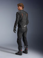 Giacca in pelle Alpinestars Dusk Airflow, nero con accenti rosso fluo, vista posteriore di un pilota con abbigliamento da moto completo in pelle, inclusi pantaloni neri coordinati, guanti e stivali racing, caratterizzata da pelle traforata e loghi Alpinestars bianchi.