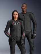 Giacca in pelle Alpinestars Stella Dusk, Nero Diva Pink Bianco, indossata da una modella accanto a un modello in abbigliamento in pelle nera coordinato, con accenti rosa e bianchi, logo a stella bianco sul petto e guanti da moto neri