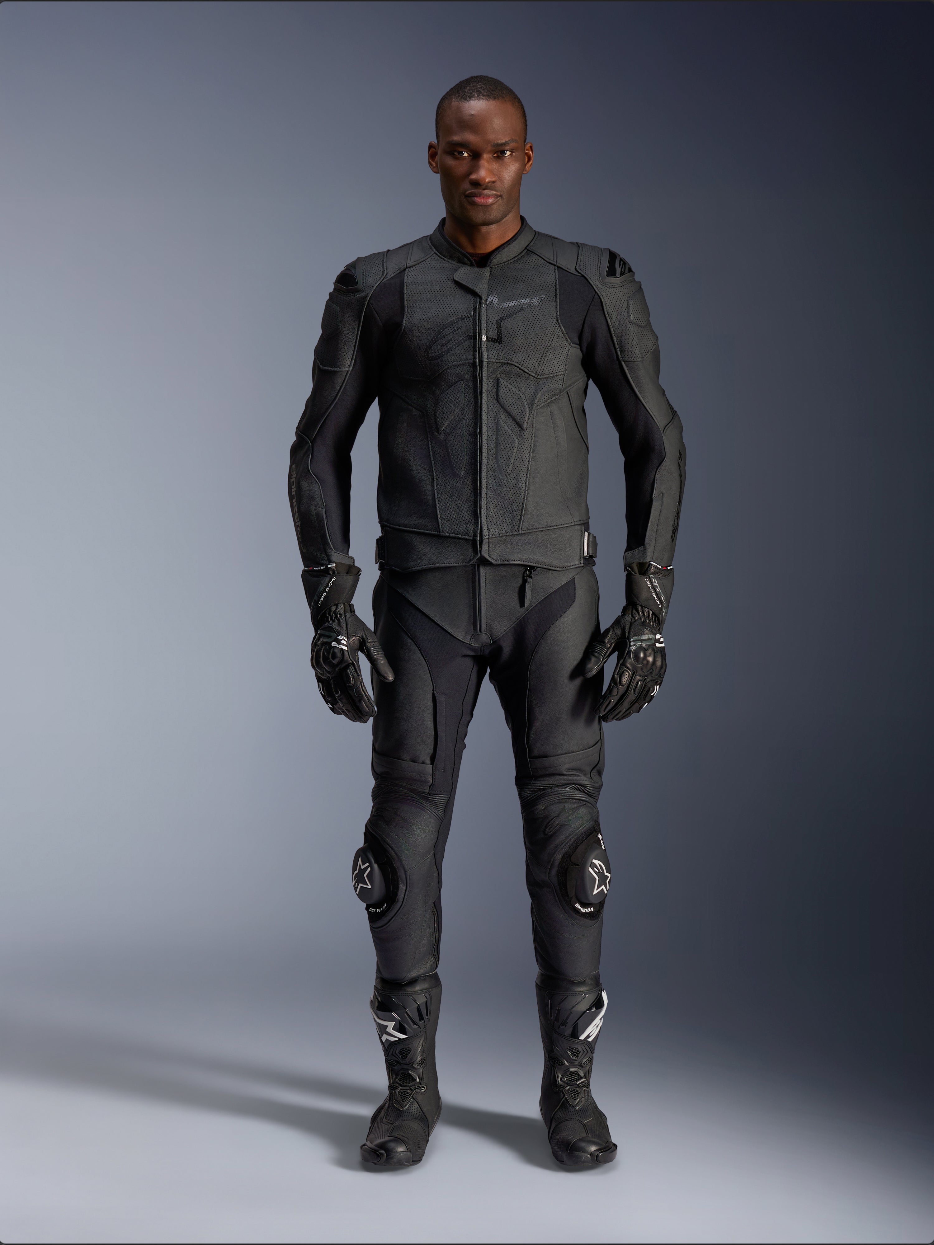 Giacca in pelle Alpinestars Dusk Airflow, nera, indossata con pantaloni da moto, guanti e stivali coordinati, caratterizzata da pelle traforata per il massimo flusso d'aria, design ergonomico multi-pannello e protezioni interne, abbigliamento professionale per guida sportiva e su strada