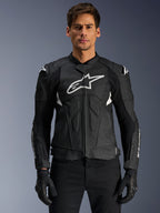 Alpinestars Dusk Airflow Leather Jacket, giacca da moto in pelle nera e bianca indossata da un modello, con pannelli in pelle traforata per la ventilazione, un grande logo bianco sul petto e slider esterni sulle spalle.