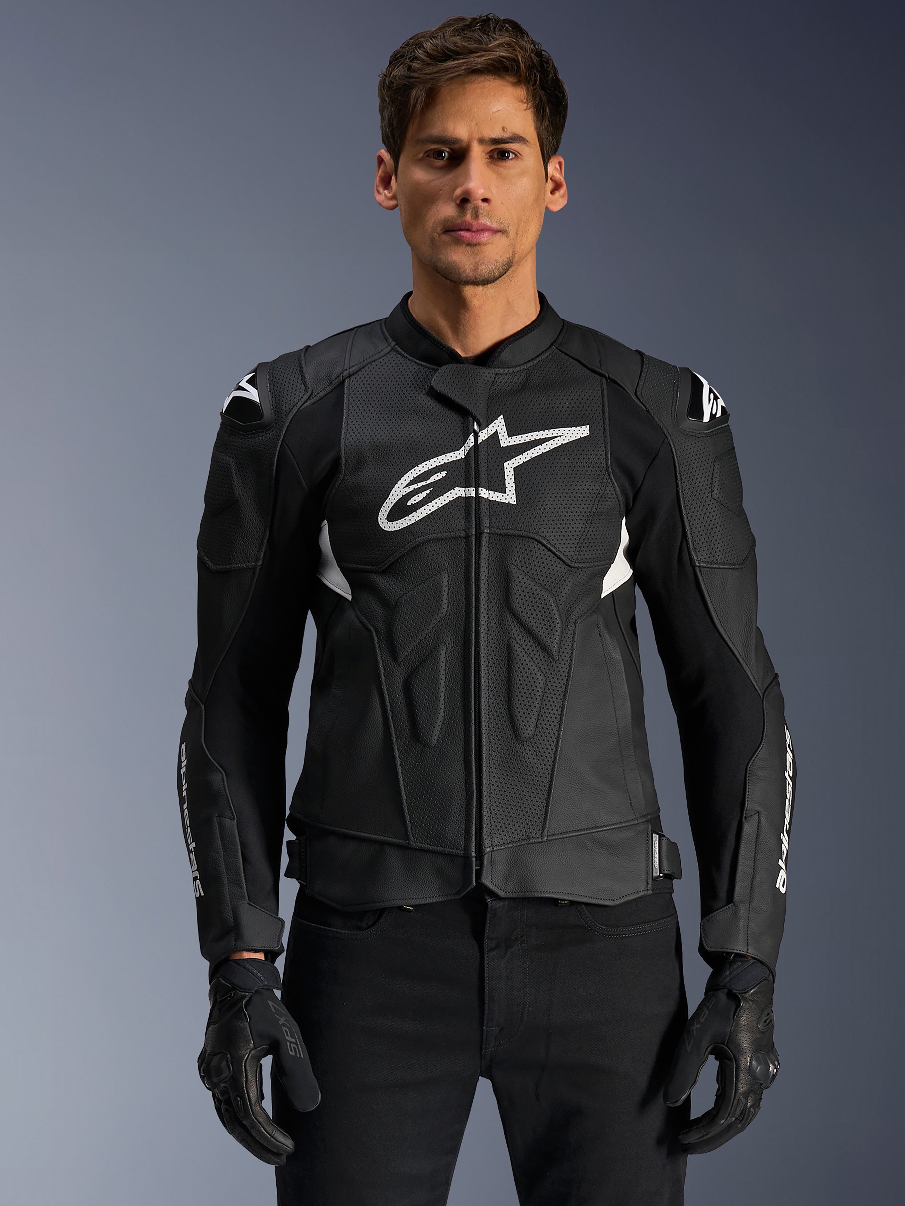 Alpinestars Dusk Airflow Leather Jacket, giacca da moto in pelle nera e bianca indossata da un modello, con pannelli in pelle traforata per la ventilazione, un grande logo bianco sul petto e slider esterni sulle spalle.