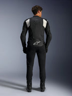 Giacca in pelle Alpinestars Dusk Airflow, nero e bianco, vista posteriore di un pilota con pantaloni e stivali neri, caratterizzata da pelle traforata per la ventilazione, pannelli a fisarmonica bianchi sulle spalle e logo bianco sulla parte bassa della schiena