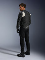 Giacca in pelle Alpinestars Dusk Airflow, nero e bianco, vista posteriore del modello che indossa la giacca in pelle traforata con pantaloni e stivali neri coordinati, caratterizzata da pannelli elastici a fisarmonica bianchi e logo sulla parte bassa della schiena, abbigliamento tecnico da moto