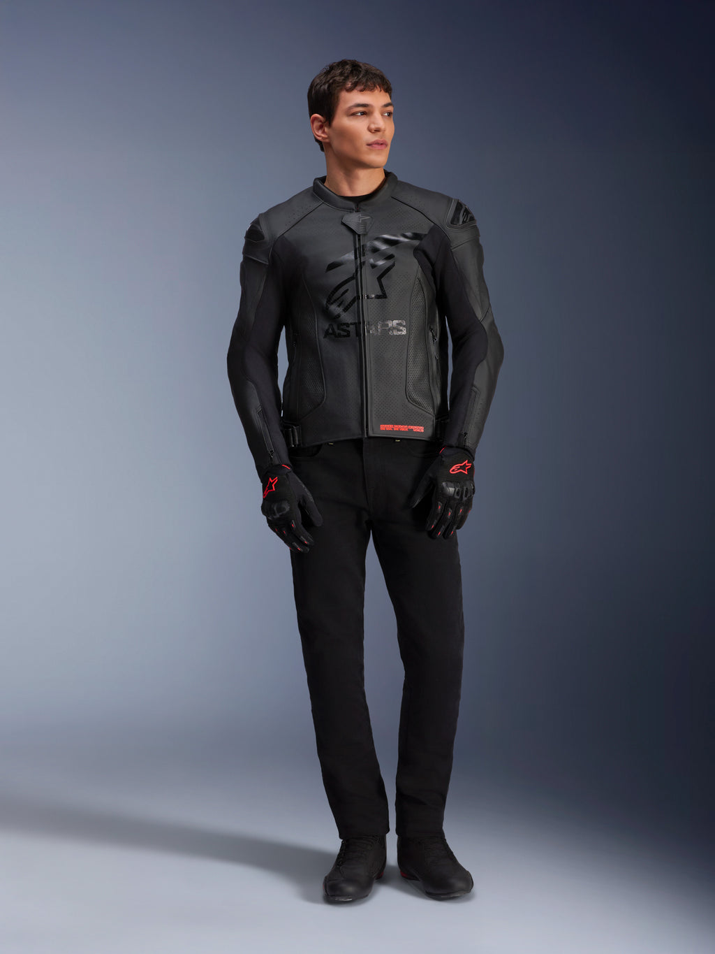 Giacca in pelle Alpinestars GP Plus R V4 Airflow, nero, indossata da un modello con guanti e pantaloni neri coordinati, caratterizzata da pannelli in pelle traforata, grande logo a stella in tono sul petto e vestibilità sportiva.