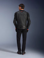 Alpinestars GP Plus R V4 Airflow Leather Jacket, nero, vista posteriore del pilota con equipaggiamento completo, pelle traforata per la ventilazione e accenti con logo rosso, design sportivo aderente, abbinata a pantaloni neri e stivali da moto