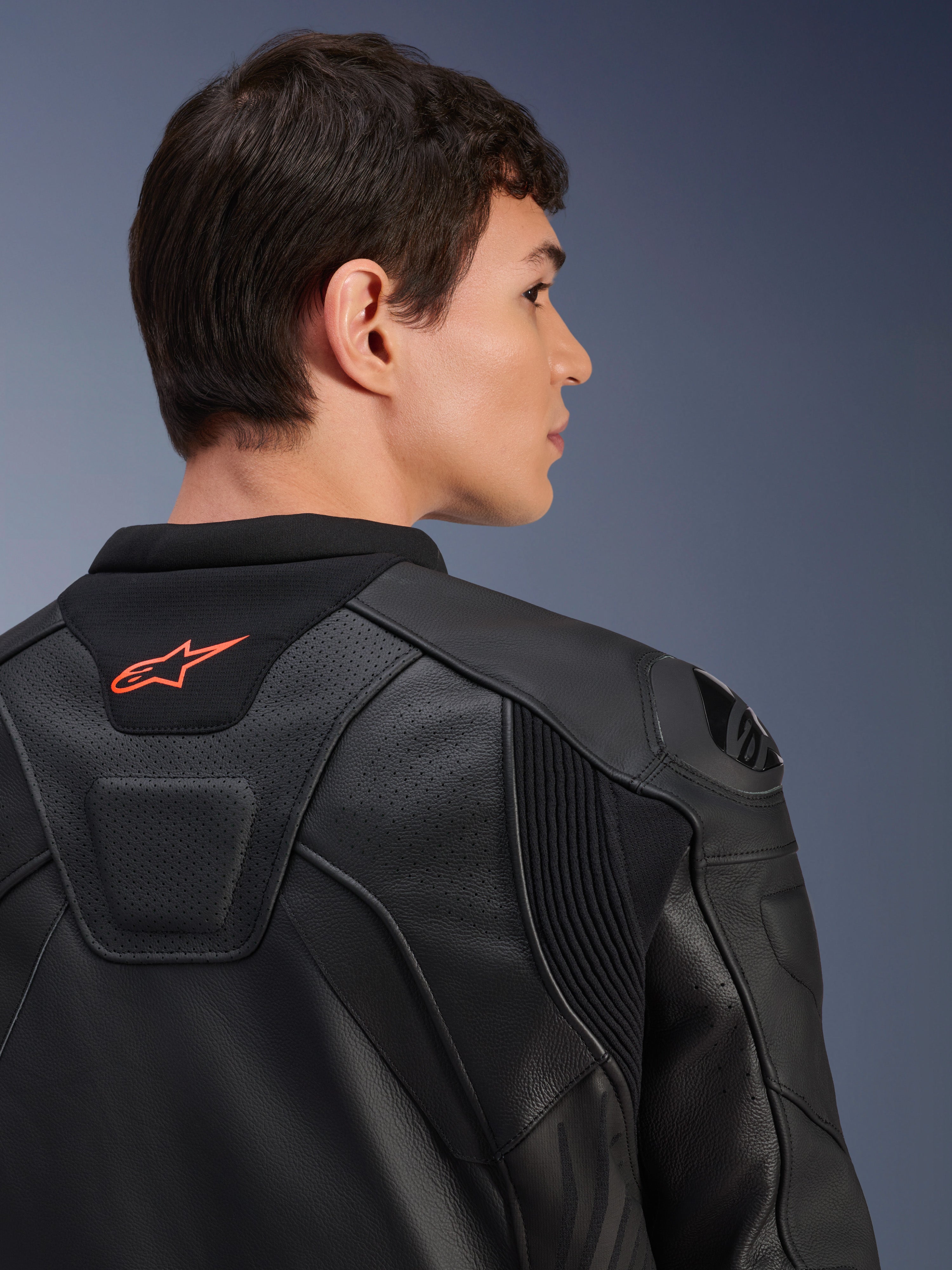 Giacca in pelle Alpinestars GP Plus R V4 Airflow, nera, vista posteriore ravvicinata su un modello, con pelle traforata di livello racing, pannelli tecnici elasticizzati e un piccolo logo Alpinestars arancione sul colletto, abbigliamento professionale da moto