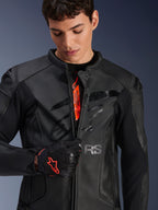 Giacca in pelle Alpinestars GP Plus R V4 Airflow in nero, modello maschile che apre parzialmente la zip frontale mostrando il marchio interno arancione, caratterizzata da pannelli in pelle traforata e logo lucido sul petto, abbinata a un guanto da moto nero e rosso