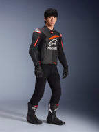 Pilota che indossa la giacca in pelle Alpinestars GP Plus R V4 Airflow, nero con accenti rosso fluo e bianco, con pelle traforata e logo ASTARS sul petto, abbinata a pantaloni da moto neri e stivali da moto neri, abbigliamento sport performance