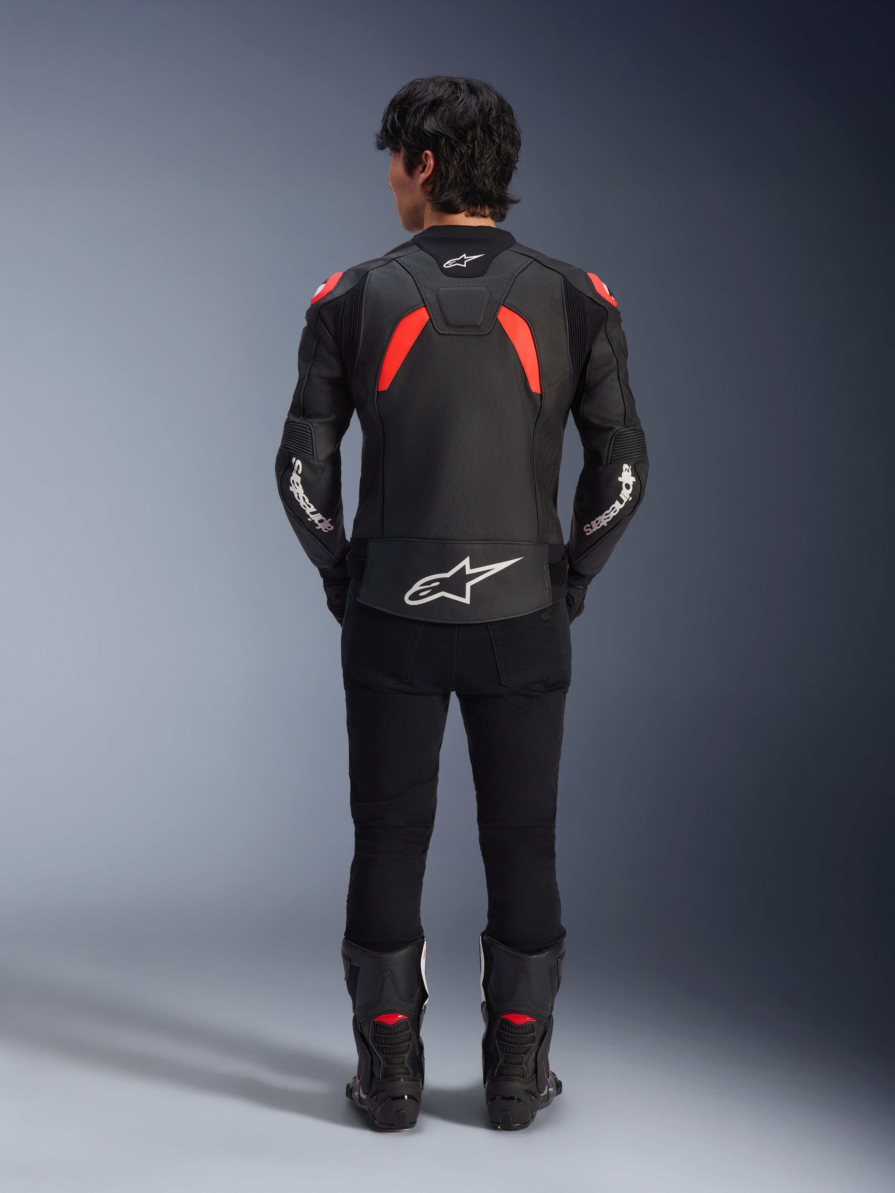Alpinestars GP Plus R V4 Airflow Leather Jacket, giacca in pelle, nero, rosso fluo e bianco, vista posteriore su un modello, caratterizzata da pannelli in pelle traforata e loghi bianchi evidenti, abbinata a pantaloni e stivali da moto neri
