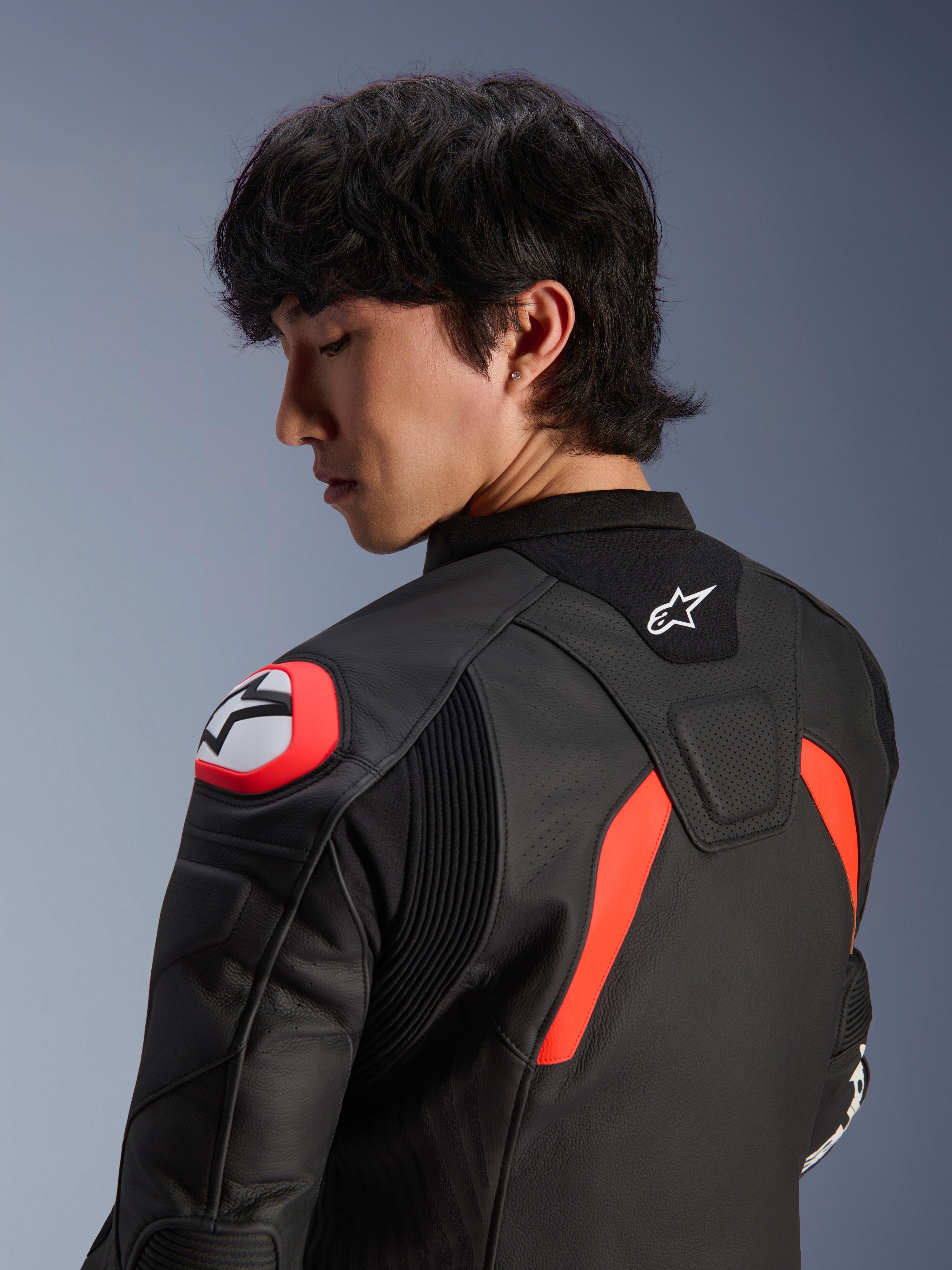 Giacca in pelle Alpinestars GP Plus R V4 Airflow, nero con dettagli rosso fluo e bianchi, vista ravvicinata della schiena e della spalla su un modello, con zone in pelle traforata, logo Alpinestars e protezione integrata sulla spalla per prestazioni motociclistiche.