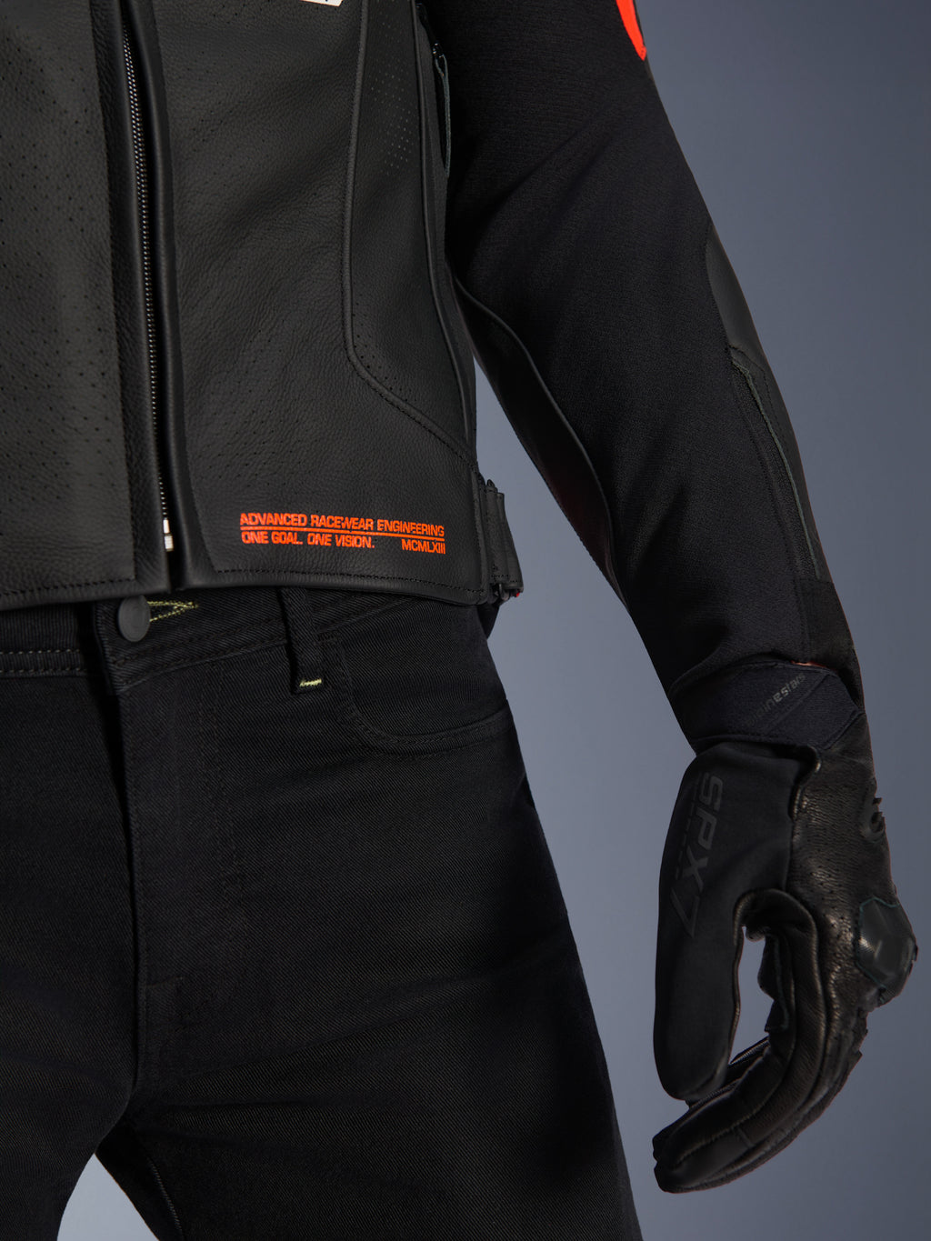 Giacca in pelle Alpinestars GP Plus R V4 Airflow, primo piano di vita e manica, pelle nera traforata con scritte in rosso fluo 'Advanced Racewear Engineering', abbinata a pantaloni da moto neri e guanto da moto SPX 7